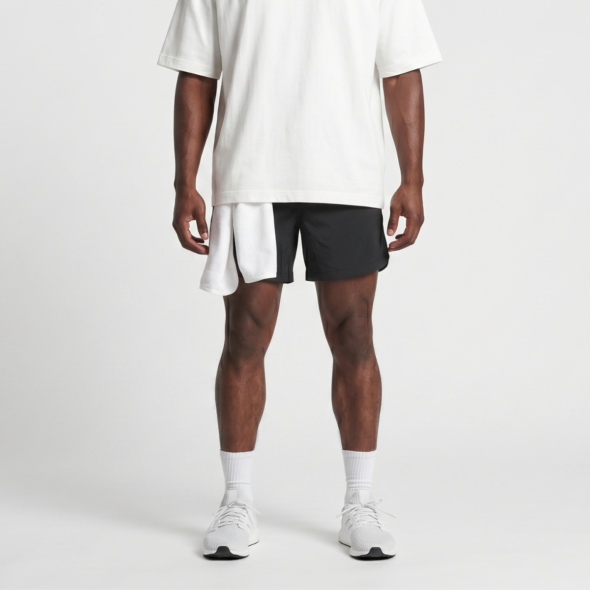 Person wearing a white oversized t-shirt, black shorts, and white sneakers on a light gray background