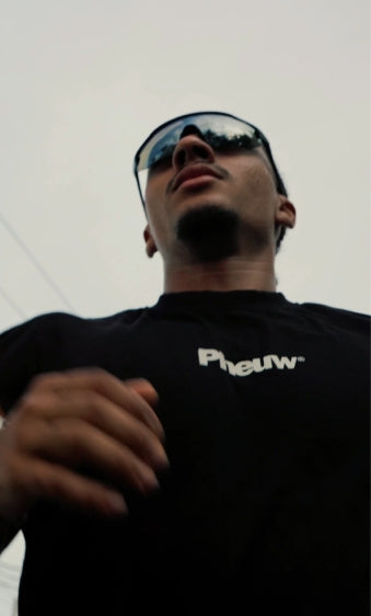 Person wearing a black shirt with 'Phew' logo and sunglasses, against a light background